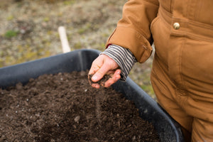 a person touching compost in a wheelbarrow